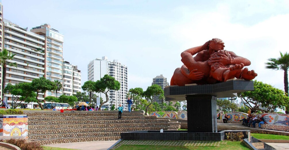 A sculpture of a reclining figure in a public park with buildings in the background. 3