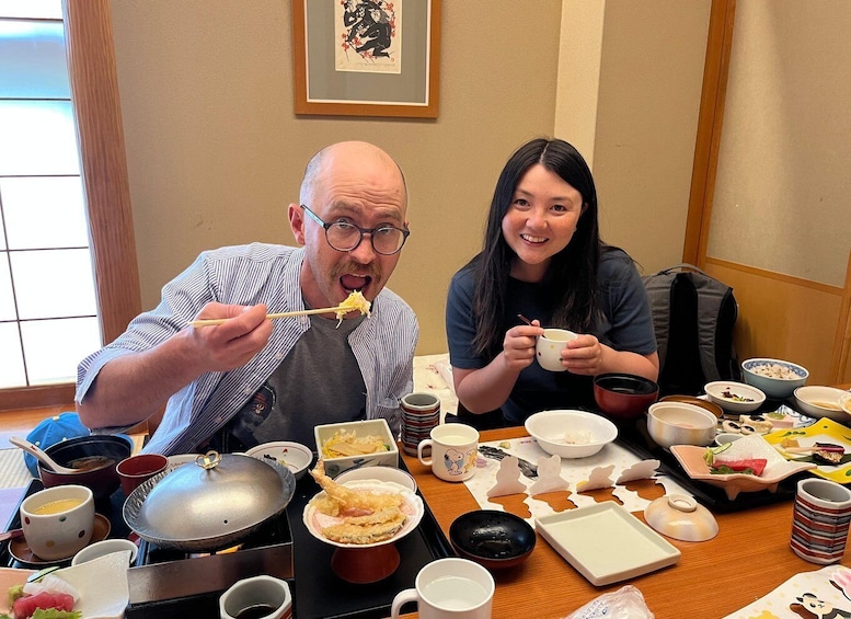 Two people dining at a table with various dishes, including sushi and bowls of soup. 1