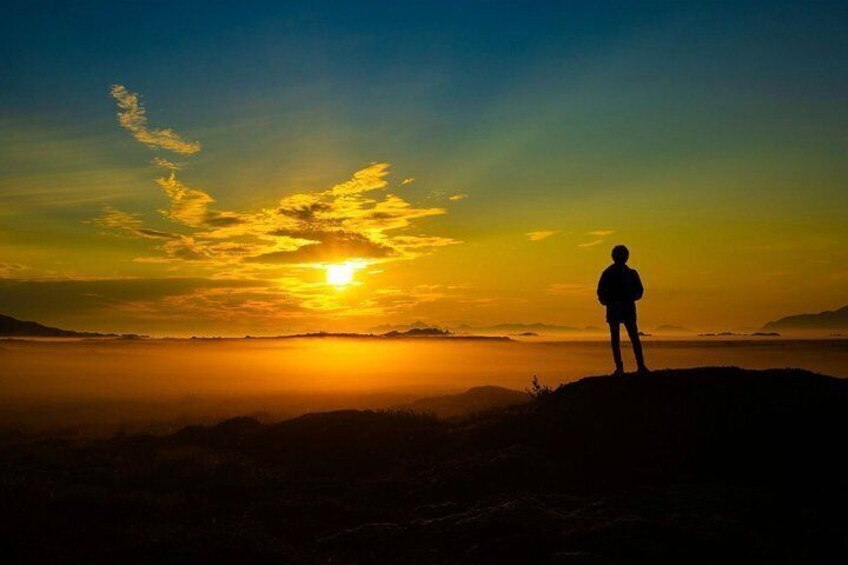A person standing on a hill overlooking a sunset with the sun near the horizon. 1