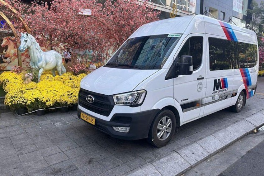 Ein weißer Van steht auf einem Bürgersteig, im Hintergrund eine Zierfigur eines Pferdes und Blumen. 1