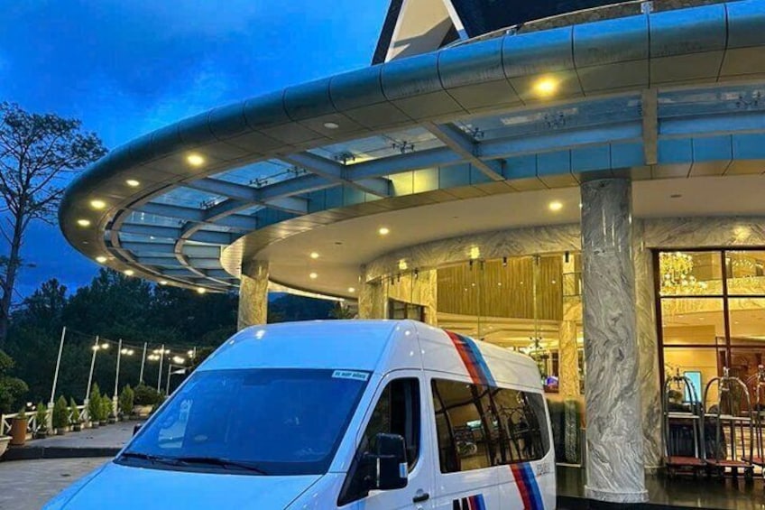 A white van parked in front of a building with a glass canopy and a marble column. 3