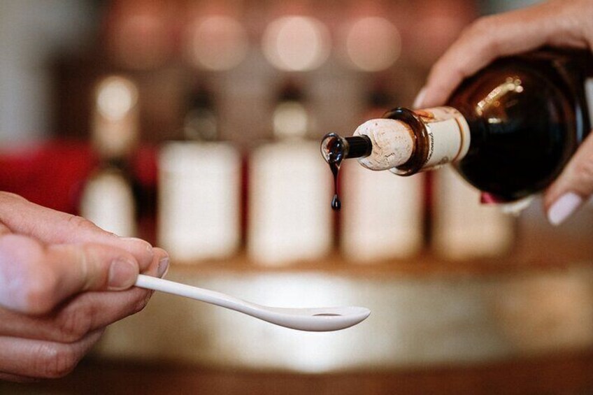 A person pouring a dark liquid from a bottle into a white spoon. 3