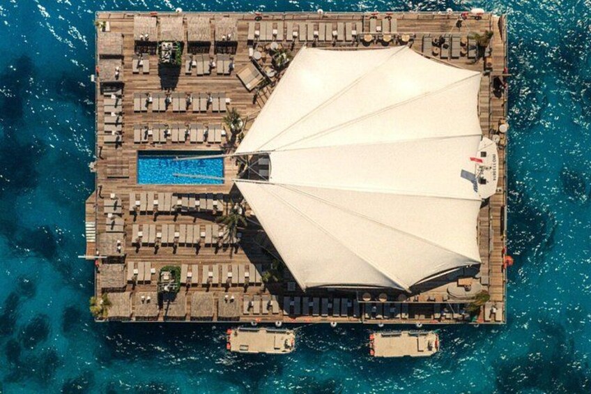 An aerial view of a resort with a large pool, sun umbrellas, and a wooden deck. 1