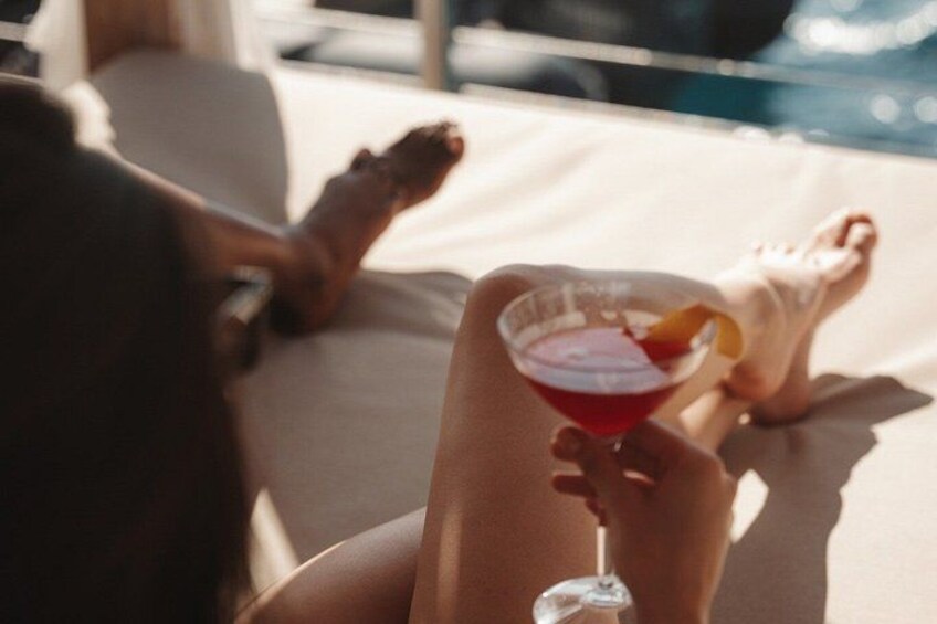 A person relaxing on a sun lounger by a pool, holding a cocktail with a garnish. 3