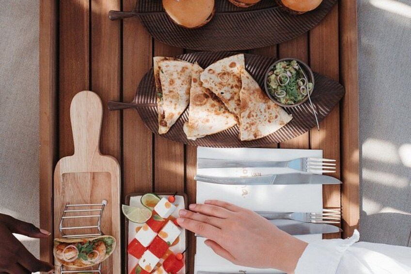 A wooden table with a plate of flatbreads, a bowl of salsa, and a cutting board with a knife. 4