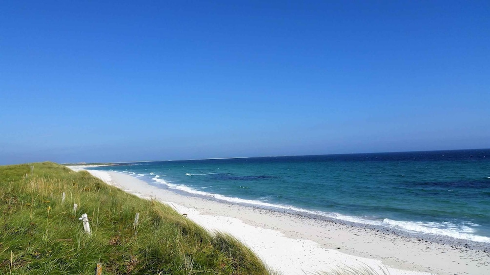 A beach with white sand, clear blue water, and grassy dunes. 2