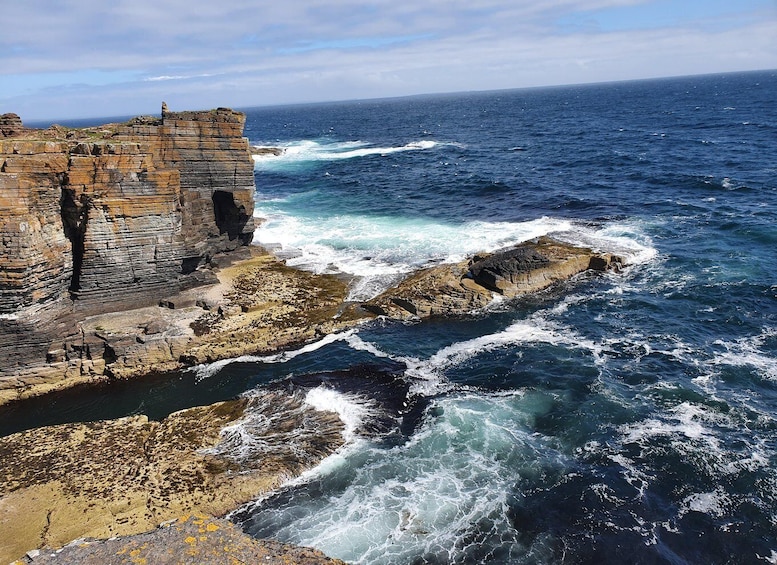 A coastal cliff with layered rock formations and waves crashing against the base. 5