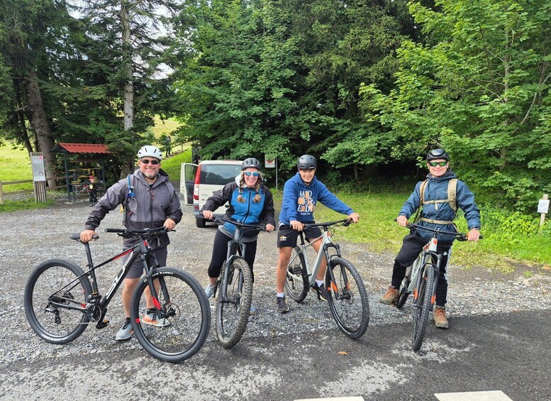 Four people on bicycles in a gravel area with trees and a parked vehicle in the background. 5