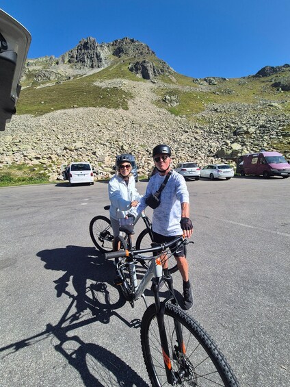 Two people with bicycles in a parking lot with mountains in the background. 2