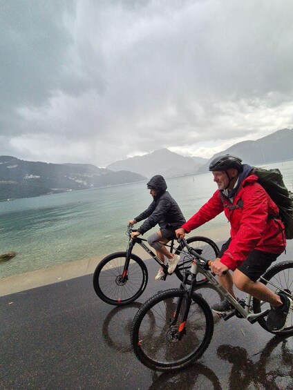 Two cyclists on a wet road with a lake and mountains in the background. 3