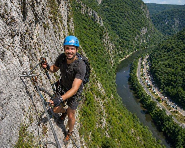 A person climbing a rocky cliff with a river and greenery in the background. 3