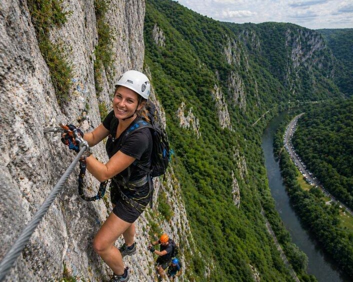 A person rock climbing a steep cliff with a river and forested valley in the background. 2