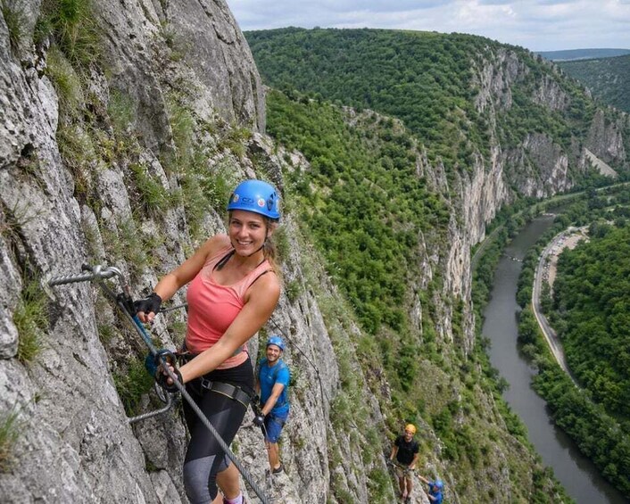 A person rappelling down a steep cliff with a river and forested valley in the background. 1