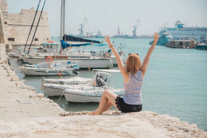 A person sitting on a stone ledge by the water, with boats docked in the background. 3