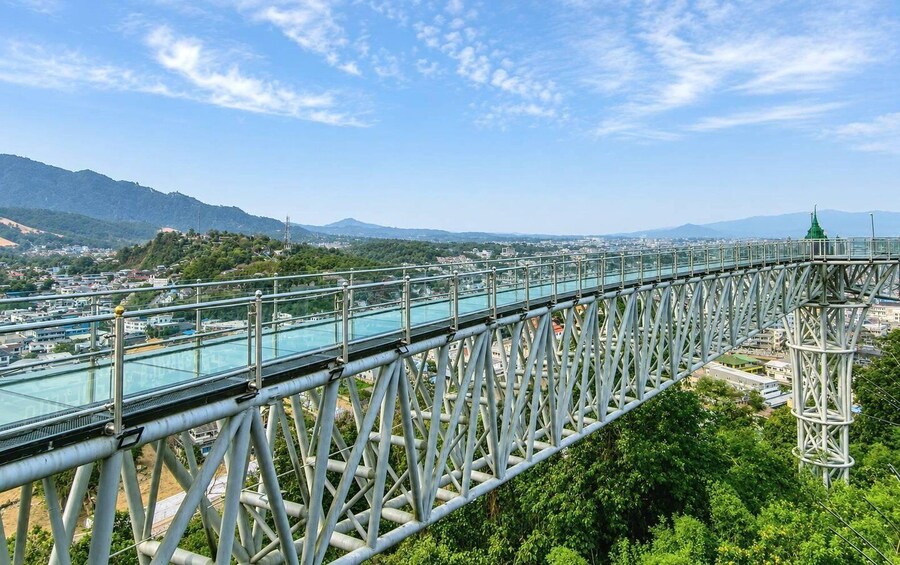 A steel bridge with glass walkways, overlooking a city and mountains. 4