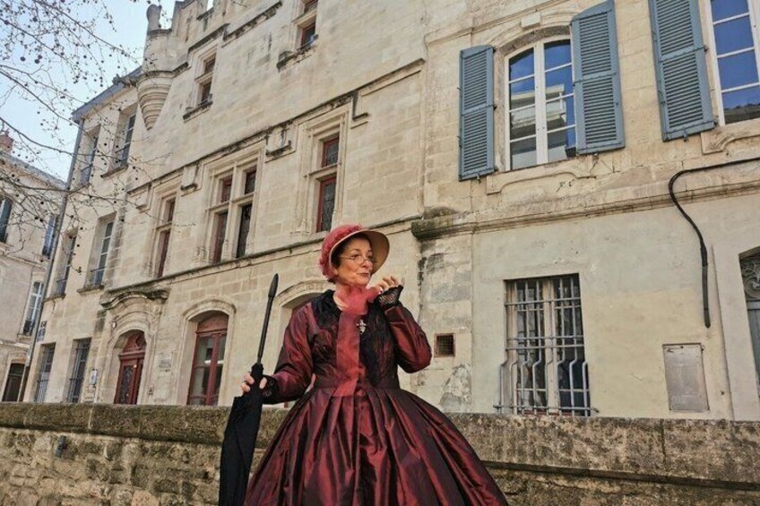 A person in a red dress standing in front of a historic building with blue shutters. 4