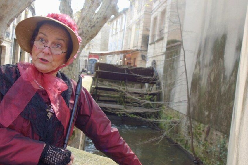 A person in a red coat and hat leaning on a stone wall with a canal and a wooden structure in the background. 3