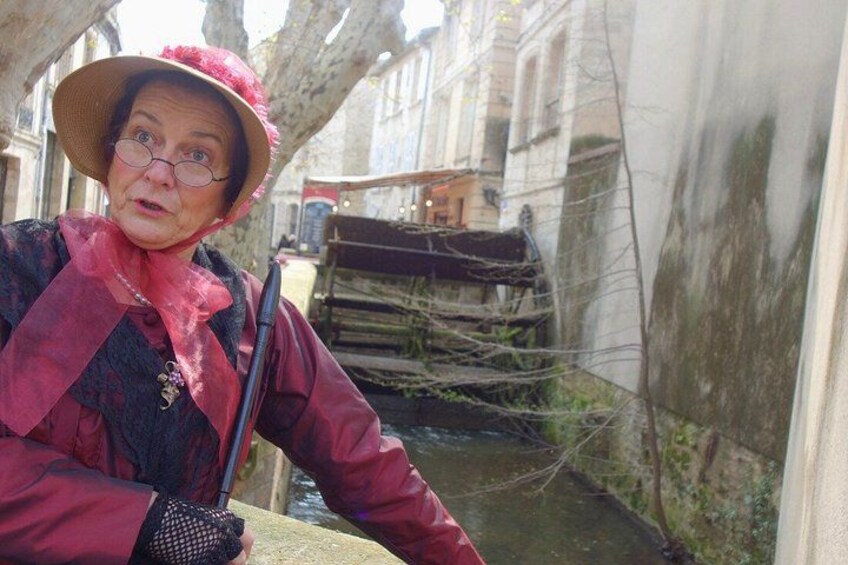 A person in a red coat and hat near a canal with a boat and buildings in the background. 3