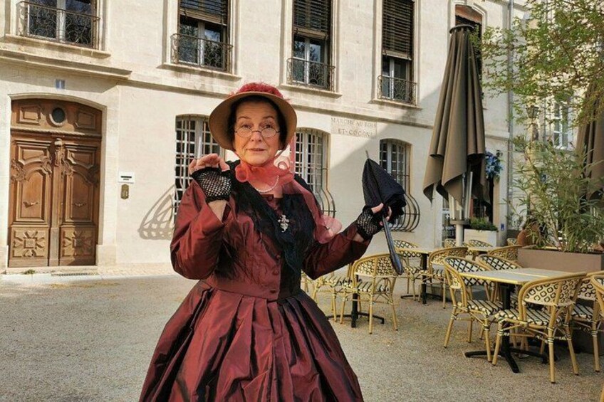 A person in a red dress and hat standing in front of a building with a door and windows. 1