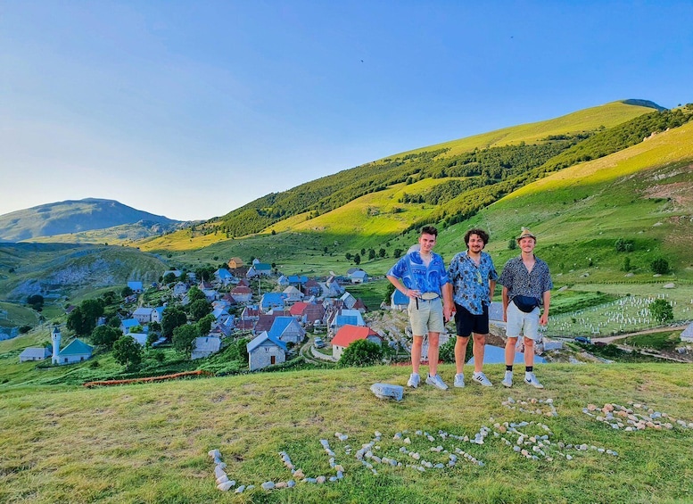 A group of people standing on a grassy hill overlooking a village with colorful houses and rolling hills in the background. 1