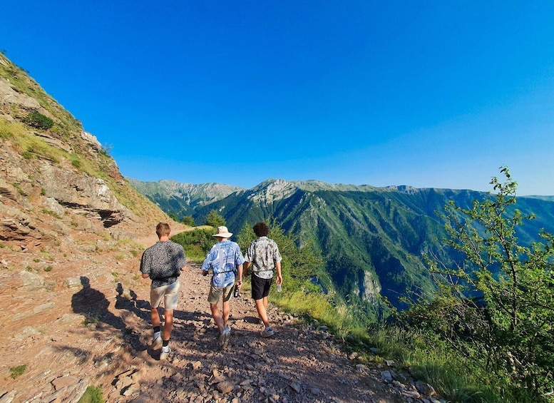 Three hikers on a rocky trail with a mountainous landscape in the background. 3