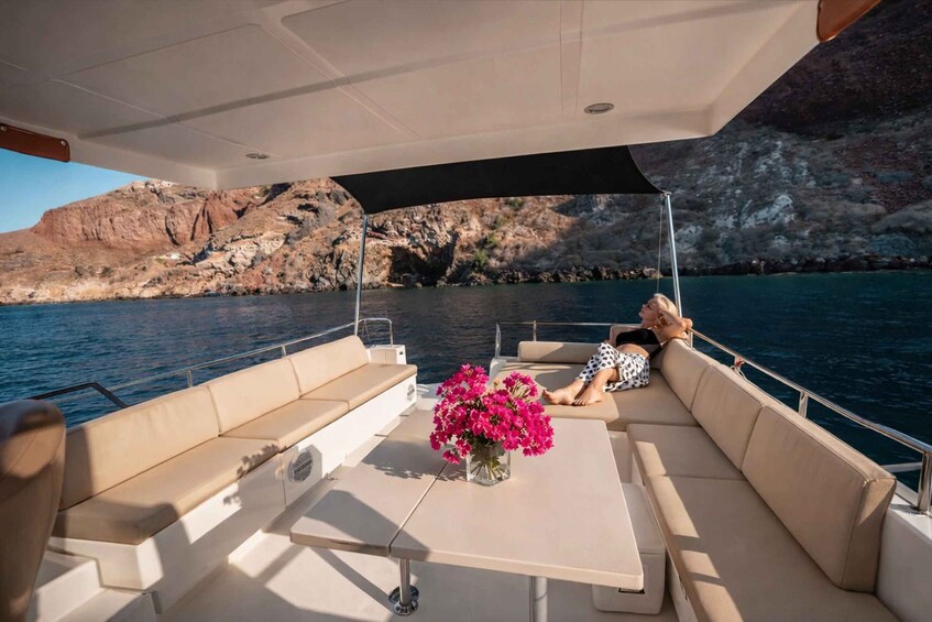 A boat with beige cushions and a table, a vase with pink flowers, and rocky cliffs in the background. 5
