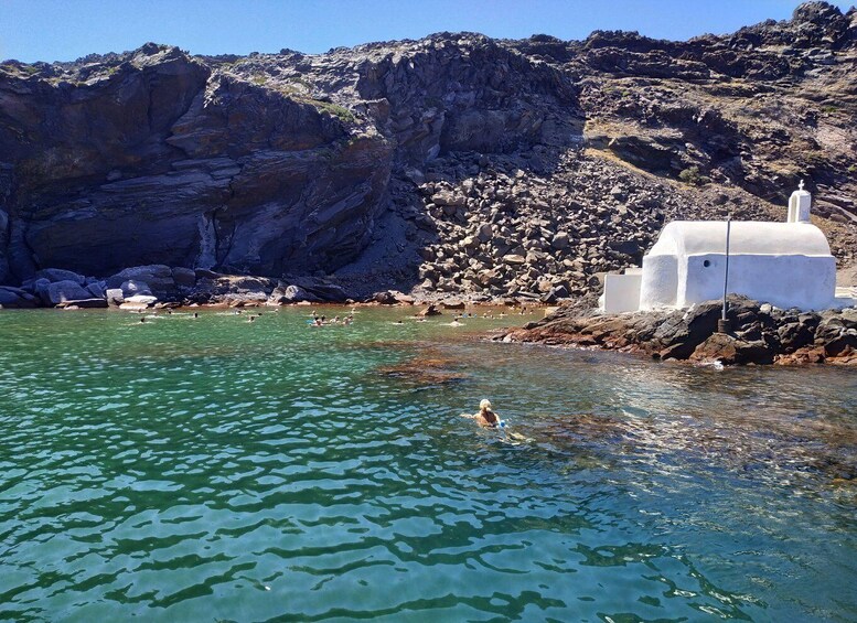 A rocky coastline with clear water, a white building, and a person swimming. 2