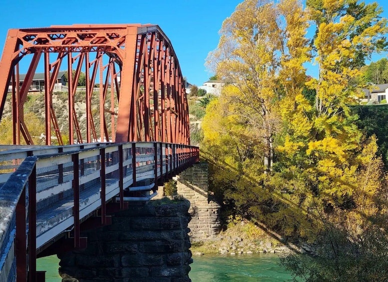 A red metal bridge over a river with autumn foliage and houses in the background. 1