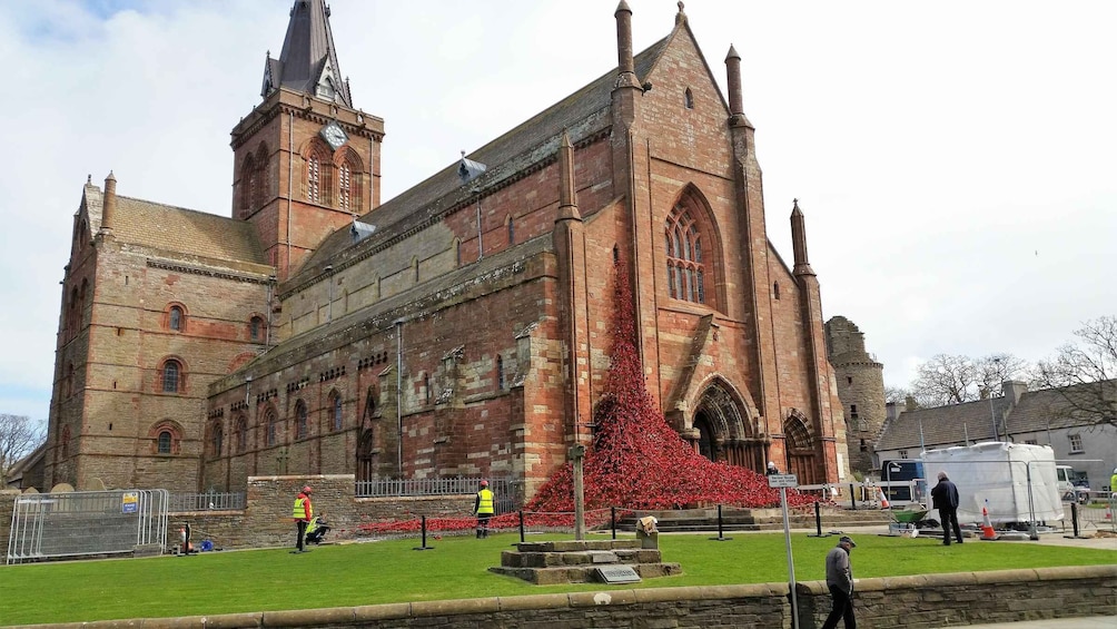 A historic church with a clock tower and a large red flower arrangement in front. 3
