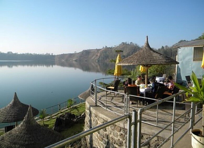 A lakeside restaurant with outdoor seating, overlooking a calm lake and a hilly landscape. 2