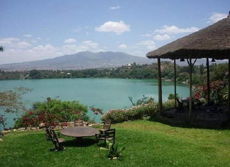 A lakeside view with a gazebo, chairs, and a table on a grassy area. 1
