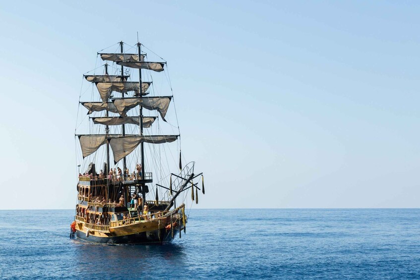 A tall ship with multiple sails and passengers on deck, sailing on calm waters. 4