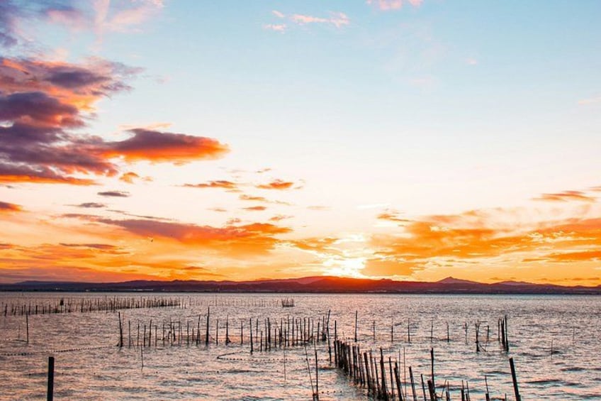 A sunset over a calm body of water with wooden posts in the foreground. 2