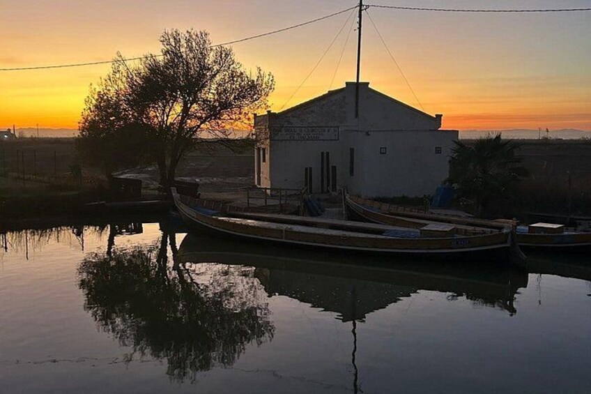 A calm river at sunset with a small building and boats. 2