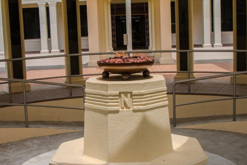 A white pedestal with a bowl of flowers on top, surrounded by a railing and columns in the background. 5