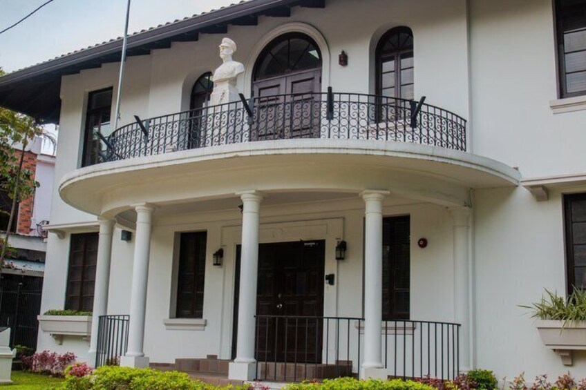 A white building with a balcony, columns, and a statue. 2