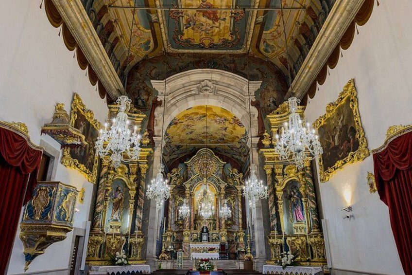 An ornate church interior with gold decorations, a central altar, and a chandelier. 2