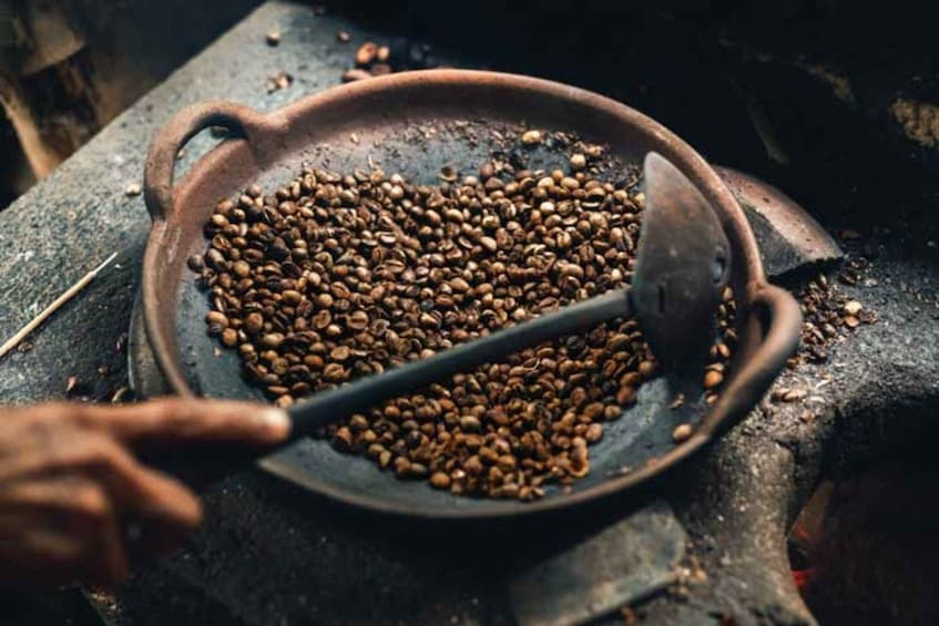 A hand stirring coffee beans in a pan. 2