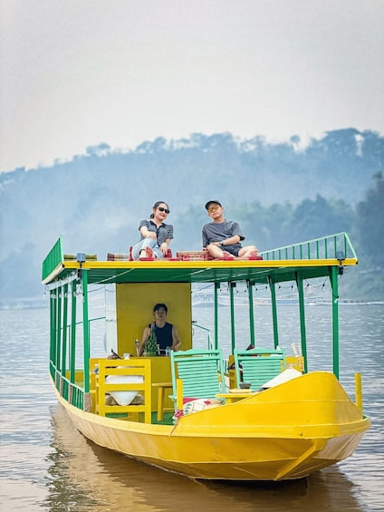 A yellow boat with two people on deck, a person driving, and a forested landscape in the background. 2