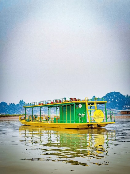 A yellow boat with a green upper deck and a sign that reads 'Banana Cruise' on a calm river. 4
