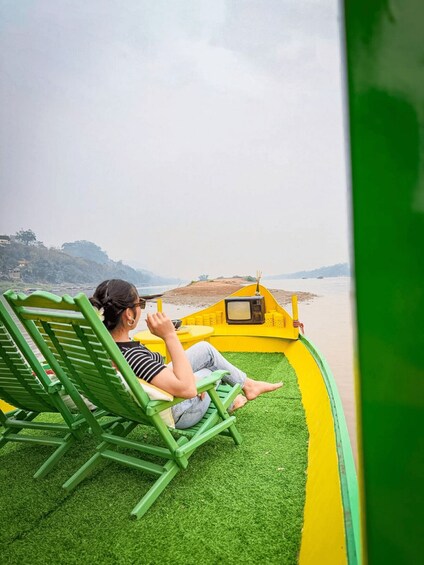 A person relaxing on a green lounge chair by a yellow boat on a grassy area. 1