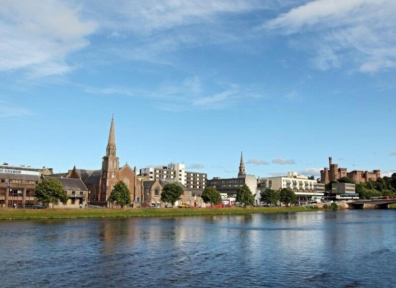 A riverside cityscape with historic buildings and a prominent church spire. 1