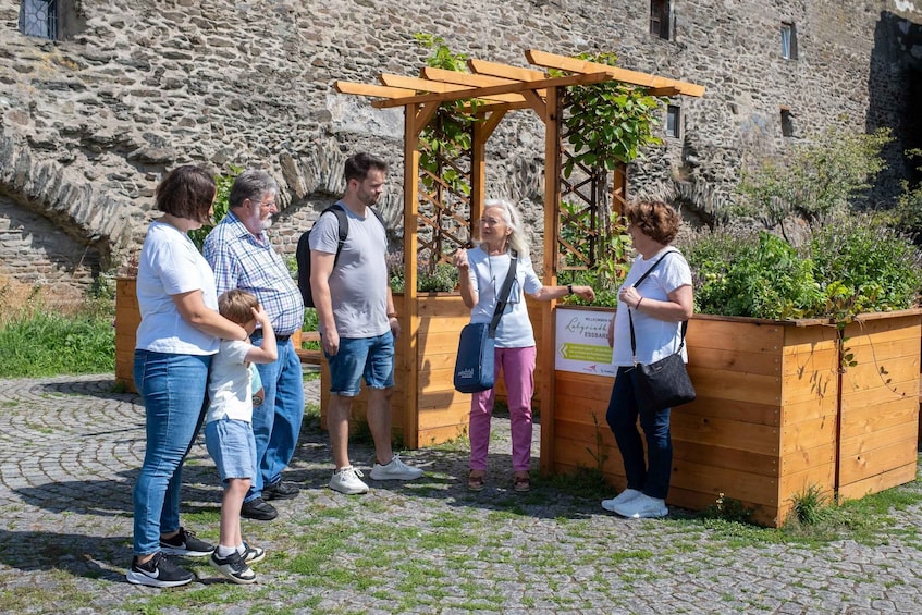 A group of people standing by a wooden structure with a sign, in front of a stone building. 3