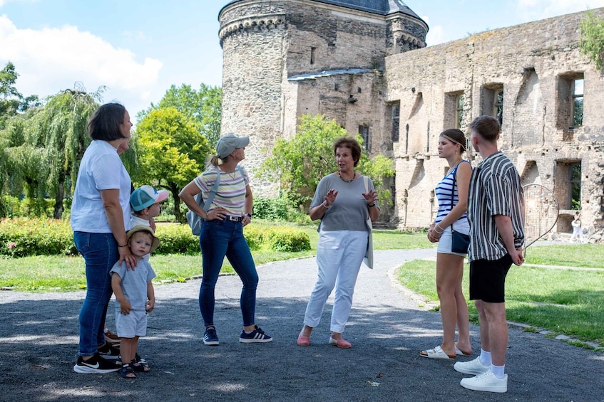 A group of people standing in a park with a historic building in the background. 1