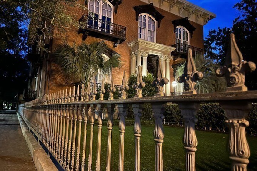 A brick house with a balcony, a well-maintained lawn, and a decorative fence. 1