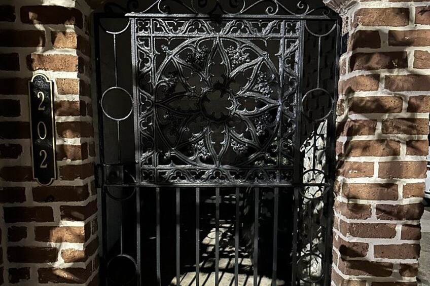 A wrought iron gate with intricate designs, a brick wall, and a number '202' sign. 3