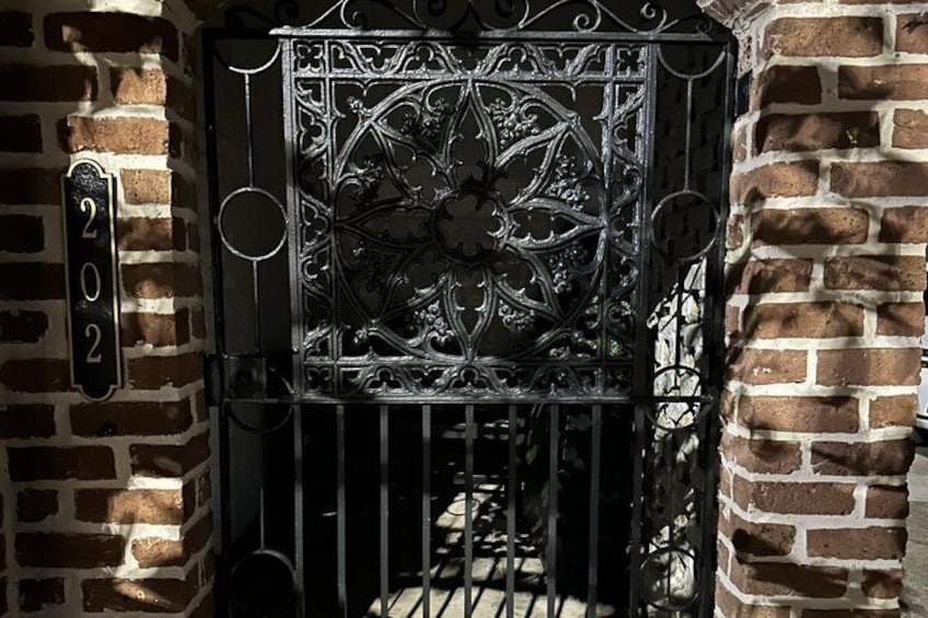 A wrought iron gate with intricate designs, a brick wall, and a number '202' sign. 3