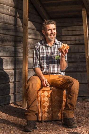 A man sitting on a wooden suitcase outdoors, holding a loaf of bread. 3