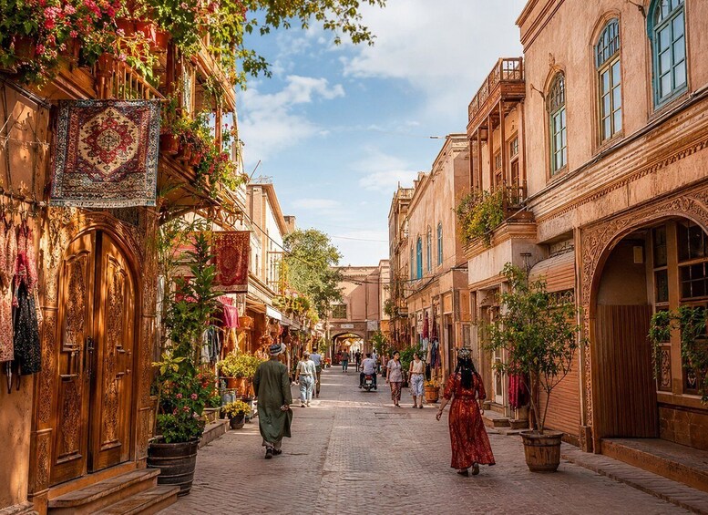 A cobblestone street lined with ornate buildings, potted plants, and hanging textiles. 2