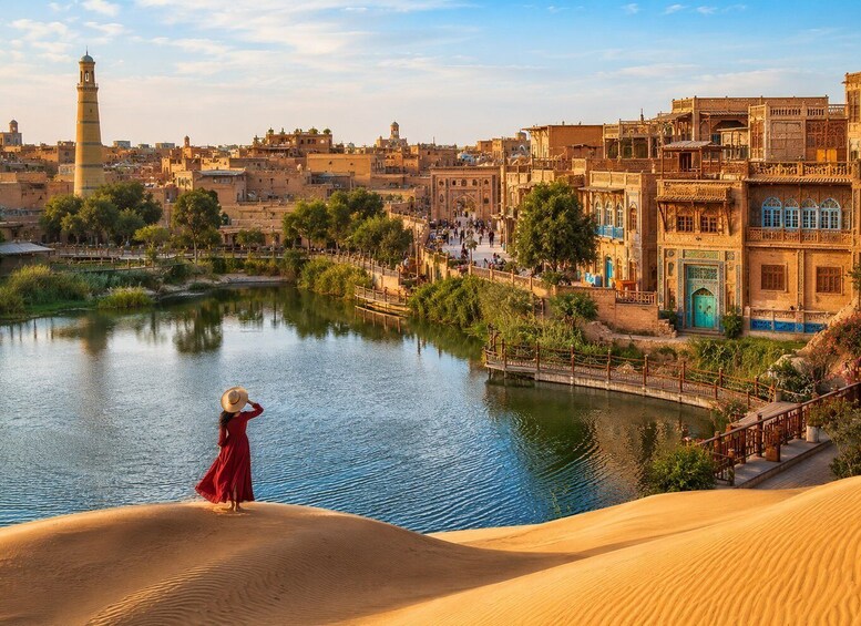 A desert landscape with sand dunes, a body of water, and traditional buildings with intricate architecture. 1